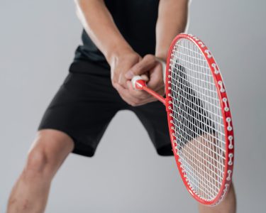 Badminton player wearing sportswear standing holding a racket in the white background.